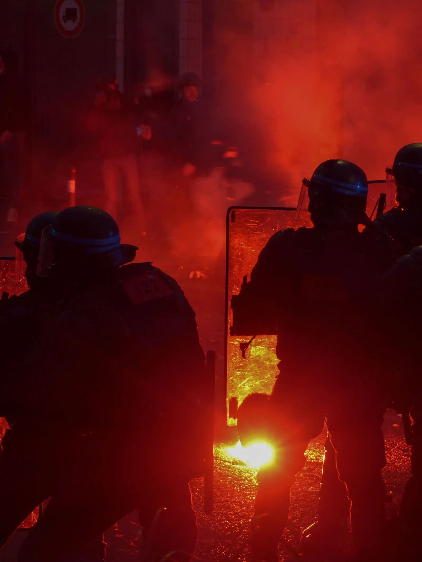 Unité de maintien de l'ordre en cordon derrière ses boucliers, éclairée par un fumigène rouge
